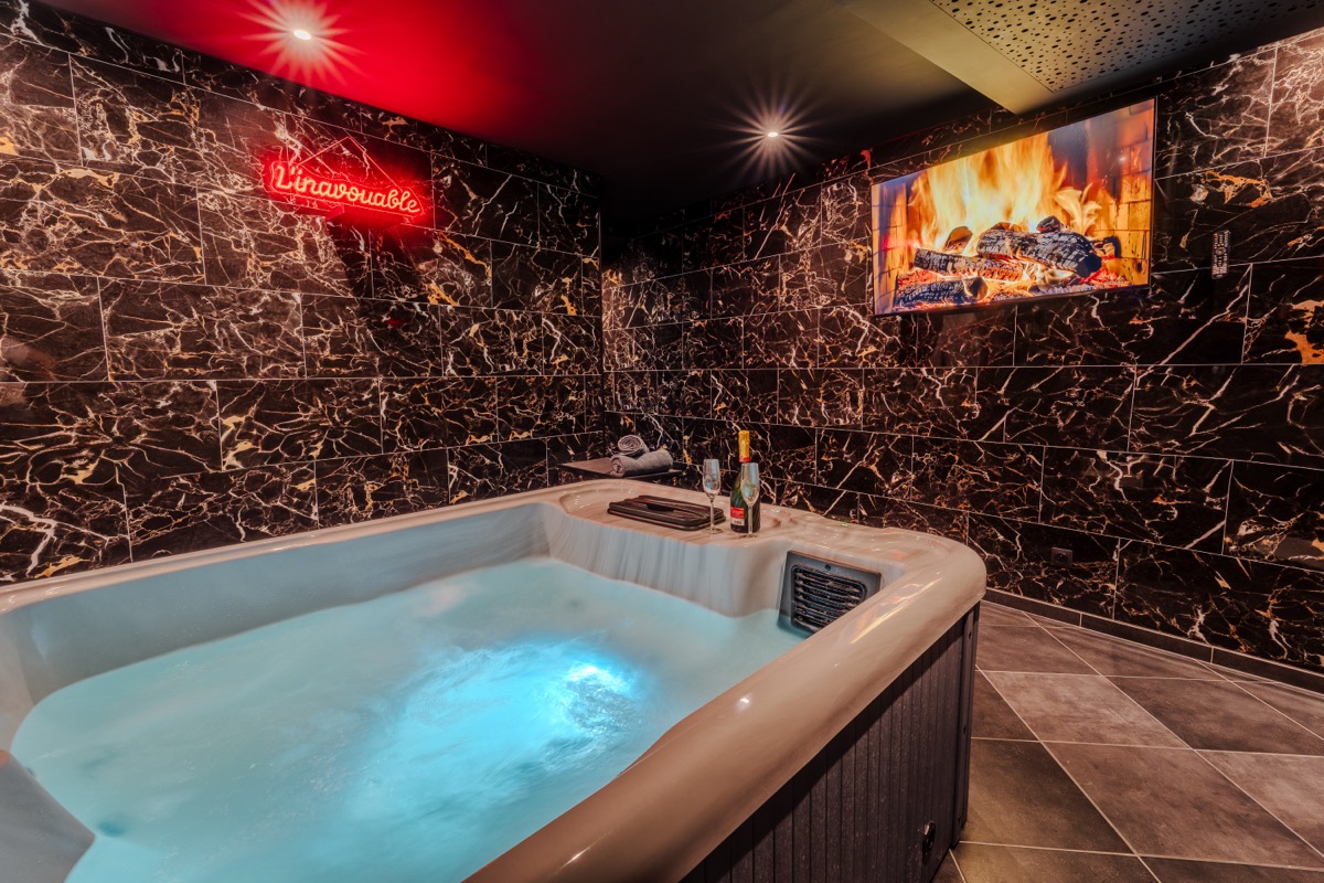 Spa privatif avec jacuzzi bouillonnant, mur en marbre noir et enseigne néon — love room L'Inavouable à Marquise